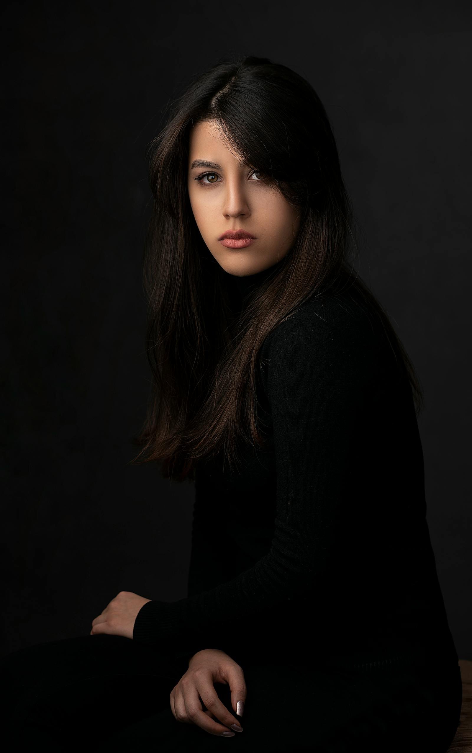 A studio portrait lit in warm tungsten — a young woman in profile against a deep charcoal seamless, soft fall-off on her shoulder, signature Brivon lighting.