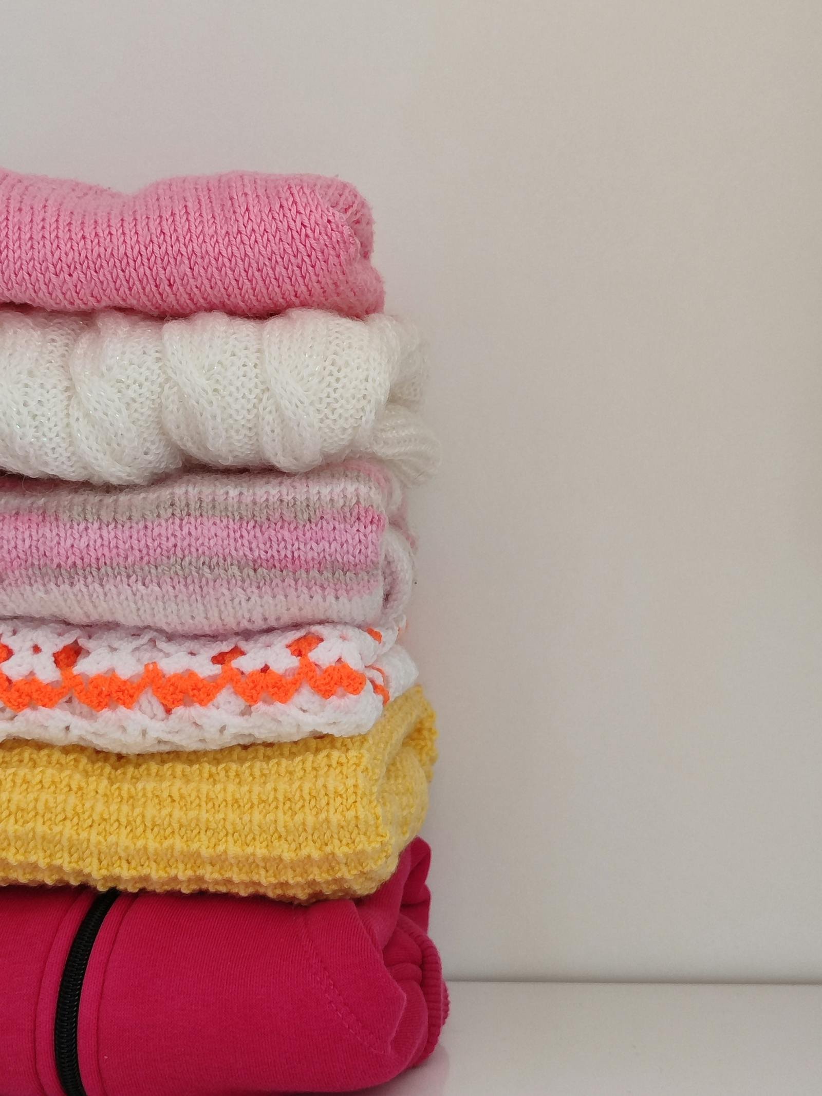 A close still of folded merino sweaters in cream, ochre, and stone — a precise stack shot under flat soft light.